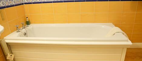 Un baño con bañera, azulejos amarillos y un borde decorativo.