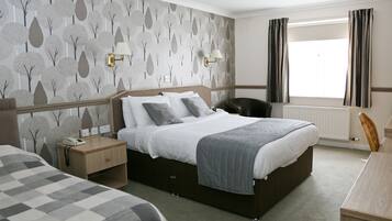 Een hotelkamer met een groot bed, een nachtkastje met een lamp, een stoel en een raam met gordijnen.