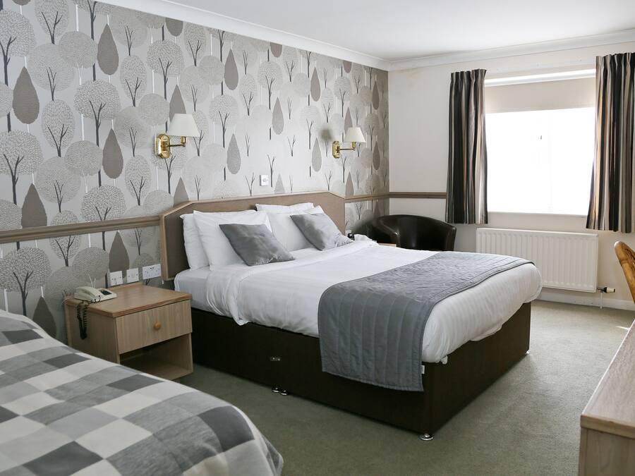 Een hotelkamer met een groot bed, een nachtkastje met een lamp, een stoel en een raam met gordijnen.