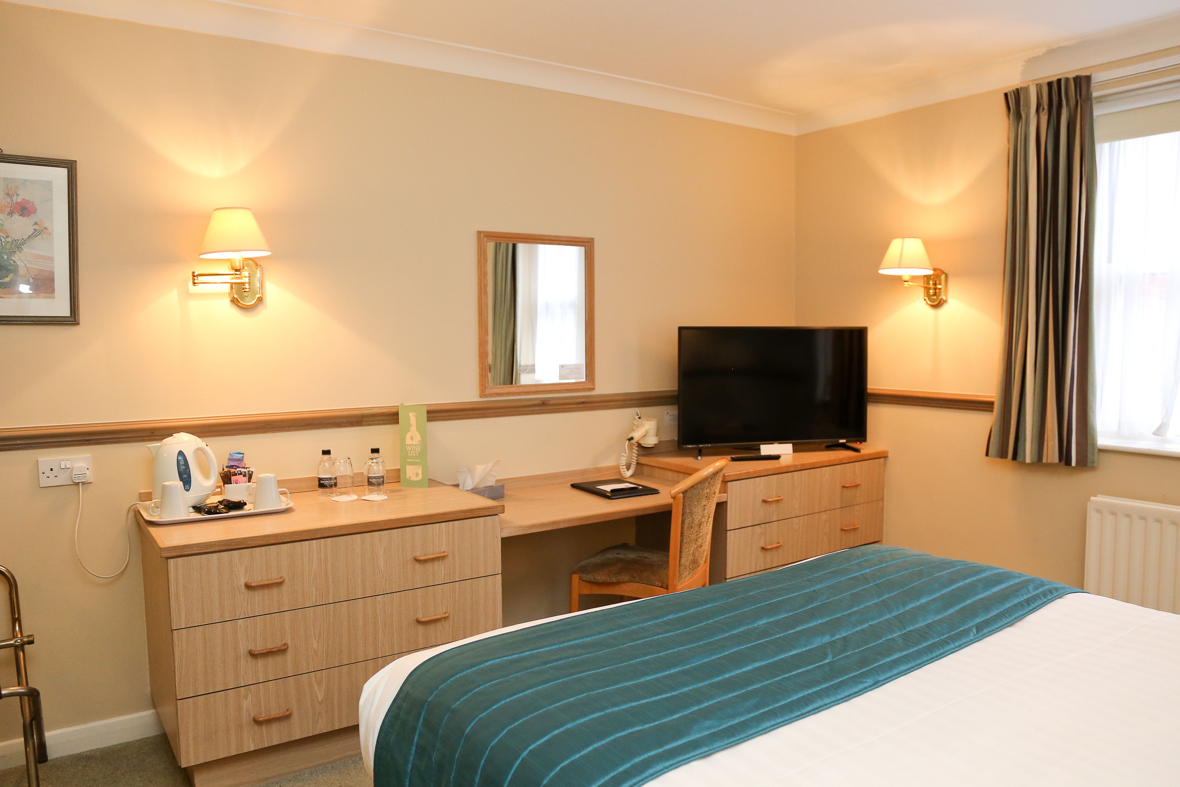 A hotel room with a bed, a desk, a chair, a television, and two wall-mounted lamps.