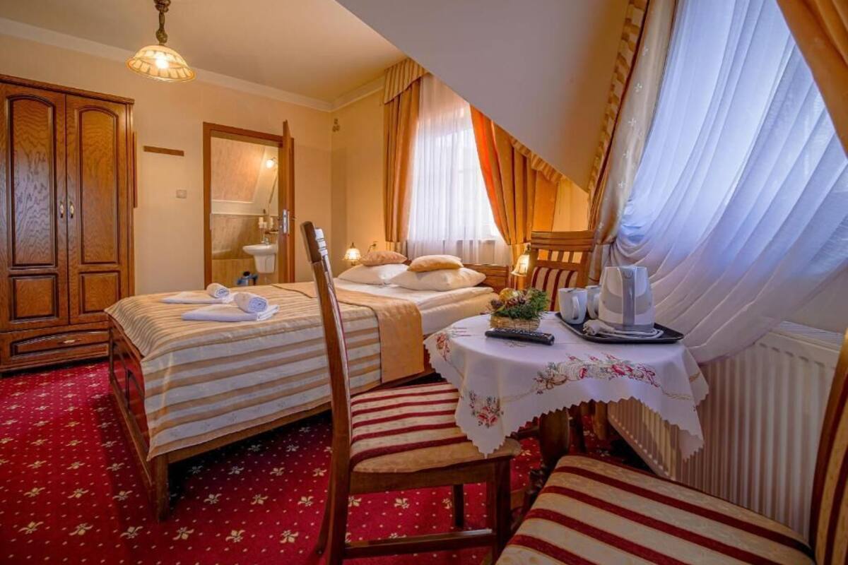 Une chambre d’hôtel avec deux lits, une table à manger recouverte d’une nappe blanche, une chaise et une fenêtre avec des rideaux.