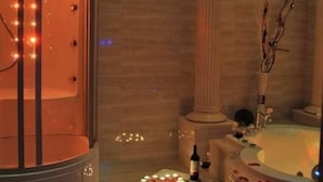 Une salle de spa avec un jacuzzi rond, une petite table sur laquelle est posée une bouteille, et des pétales de rose éparpillés.
