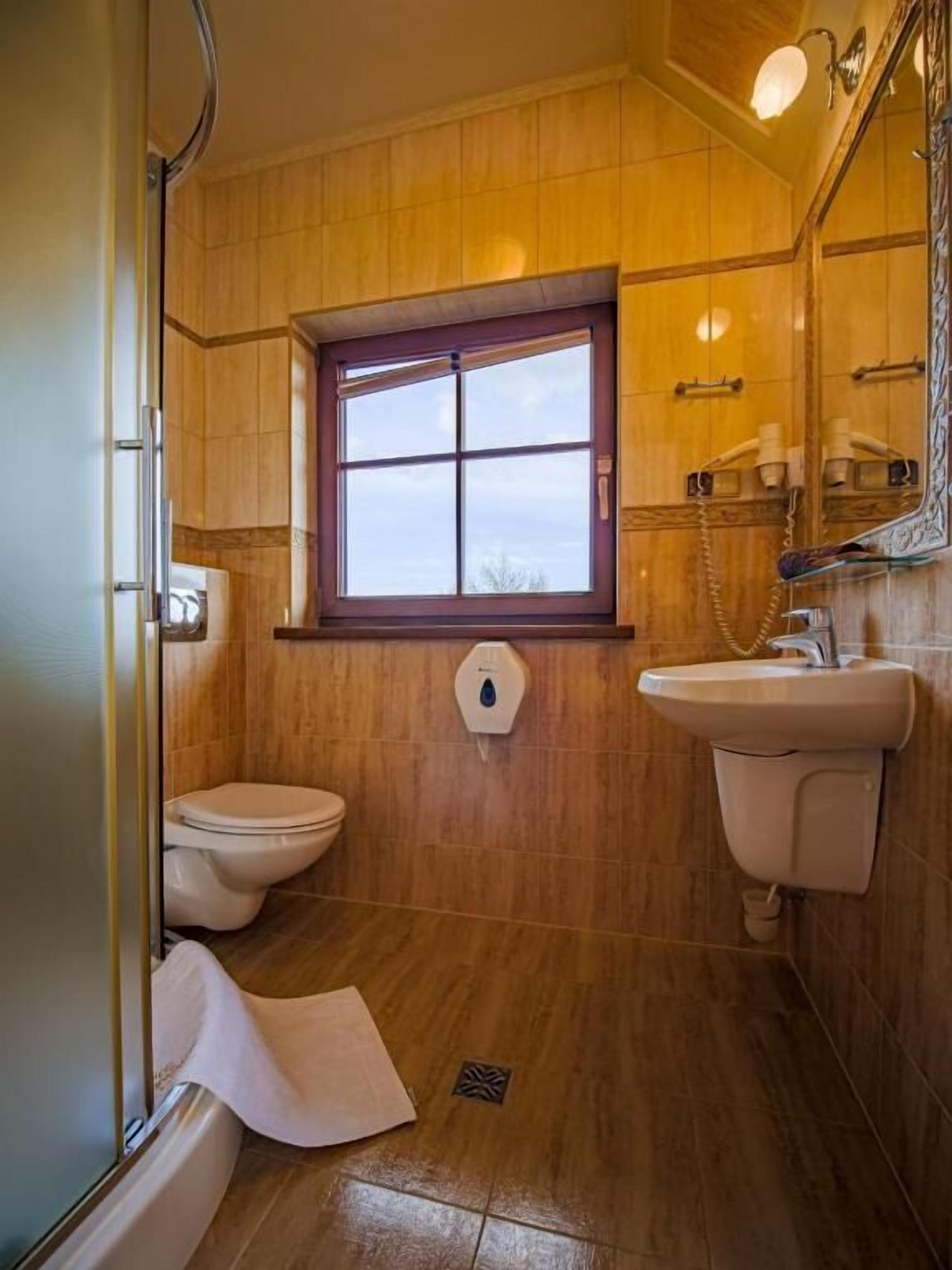 A bathroom with wooden walls, a window, a toilet, a sink, and a shower area.