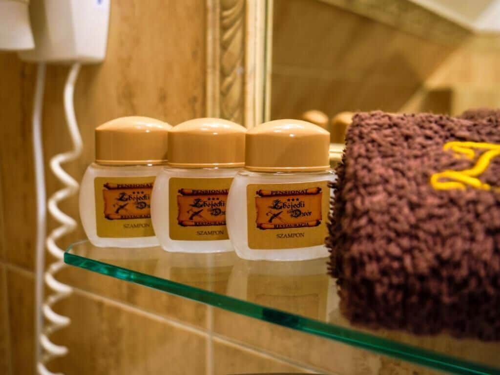 A glass shelf with three bottles of shampoo and a towel with a yellow logo.