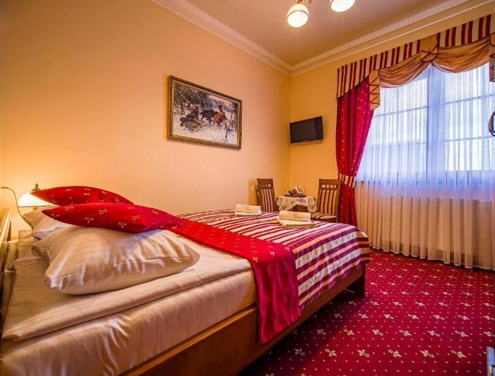 Una habitación de hotel con una cama, televisión, escritorio y ventana con cortinas.