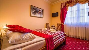 Una habitación de hotel con una cama, televisión, escritorio y ventana con cortinas.