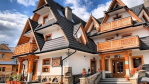 A traditional wooden building with a steeply pitched roof, multiple balconies, and a stone foundation. - Pensjonat Zbójecki Dwór (Bukowina Tatrzanska)