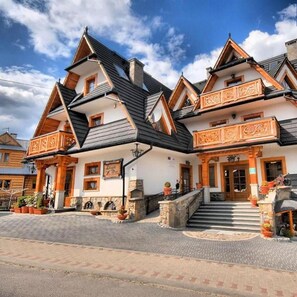 A traditional wooden building with a steeply pitched roof, multiple balconies, and a stone foundation. - Pensjonat Zbójecki Dwór (Bukowina Tatrzanska)