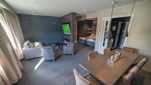 Une chambre d’hôtel moderne dotée d’une grande télévision à écran plat, d’un coin repas avec une table et des chaises en bois, d’un canapé et d’un lit avec une table de chevet.