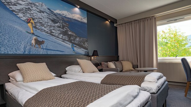 Une chambre d’hôtel avec deux lits, un grand téléviseur fixé au mur qui diffuse une image de montagnes enneigées, une petite table et une chaise.