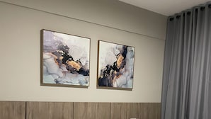 Hotellihuone, jossa on s änky, kaksi yöpöytää, yölamppu ja kaksi abstraktia maalausta seinällä.