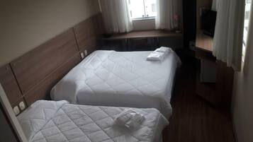 Een hotelkamer met twee bedden, een houten hoofdbord, een bureau, een stoel, een televisie en een raam met gordijnen.