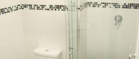 Un baño con inodoro, ducha con puerta de cristal y suelo de baldosas negras.