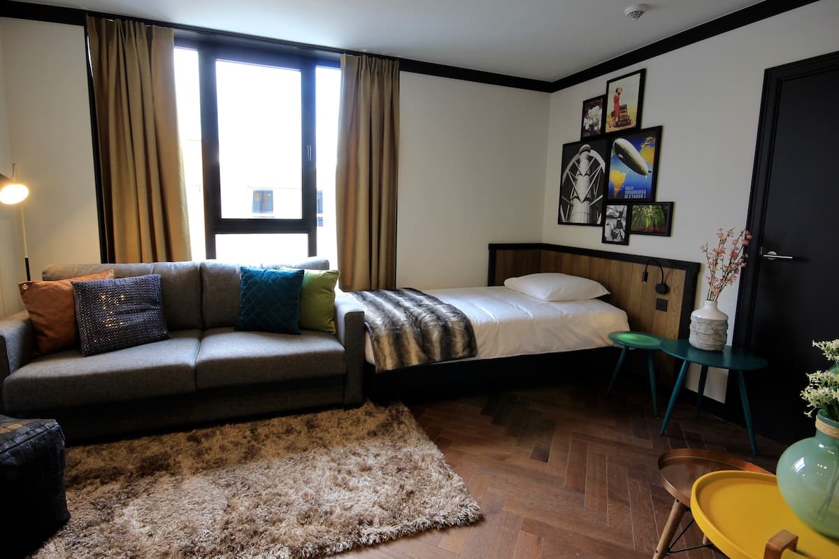 Una habitación de hotel moderna con sofá, cama y una mesita con un florero.
