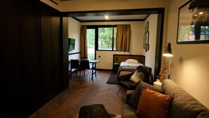 A cozy room with a bed, a sofa, a desk, and a chair. There is a window with curtains, a lamp, and a framed picture on the wall.