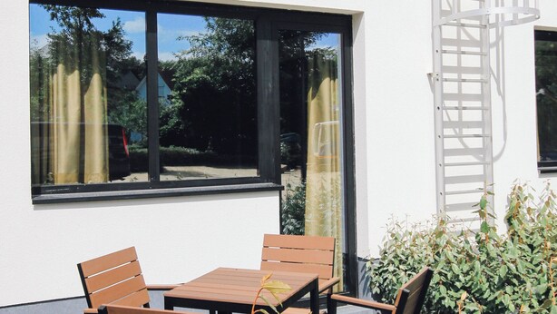 Un bâtiment moderne doté d’un balcon, de grandes fenêtres et d’un espace extérieur aménagé pour s’asseoir.