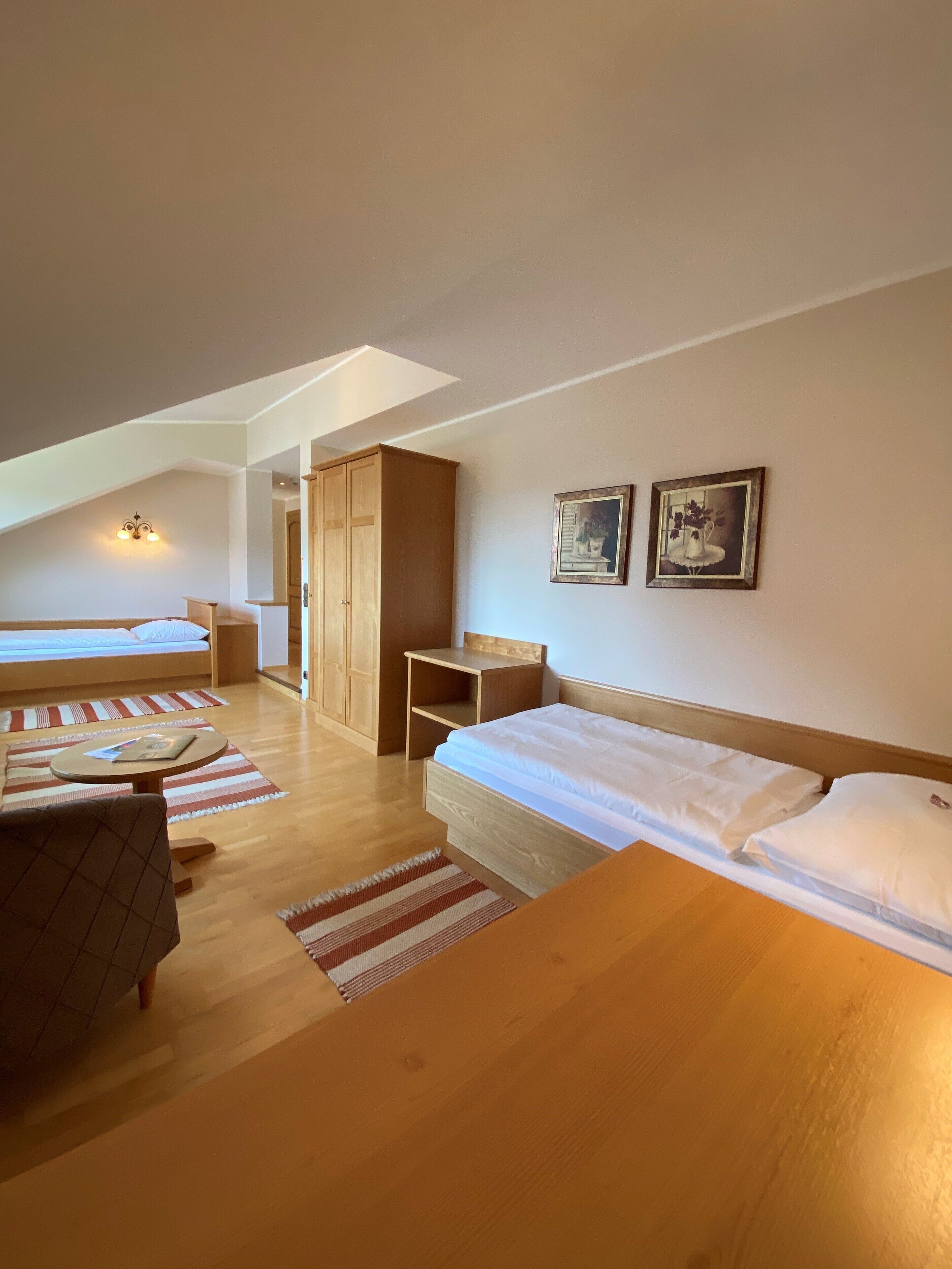 Una habitación amplia con una cama estilo altillo, un escritorio de madera y una pequeña mesa. Hay dos cuadros en la pared.