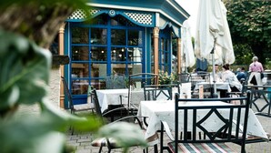 An outdoor dining area with tables and chairs, a blue building with large windows, and white umbrellas. - Gasthof Schorn (Groedig)