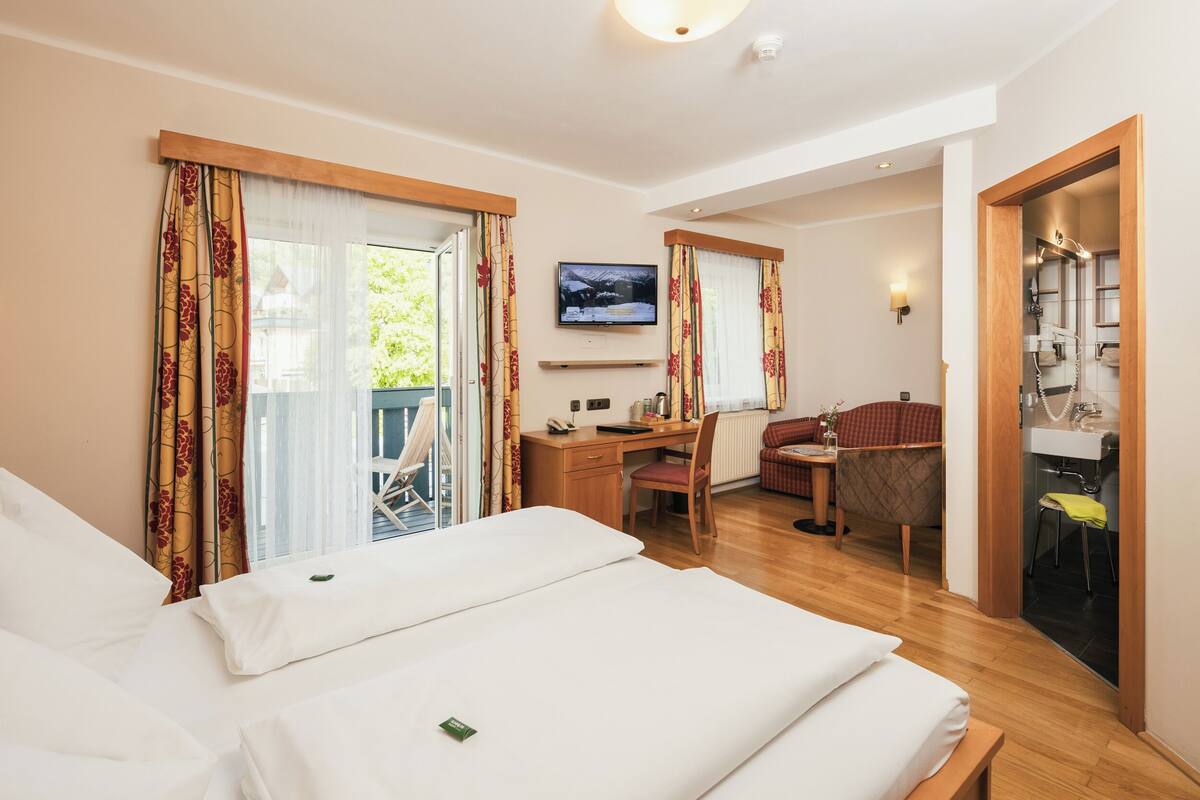 A hotel room with a bed, desk, chair, and a TV mounted on the wall.