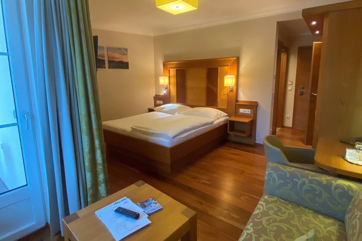 A hotel room with a bed, a wooden table, a sofa, and a bathroom visible through an open door.