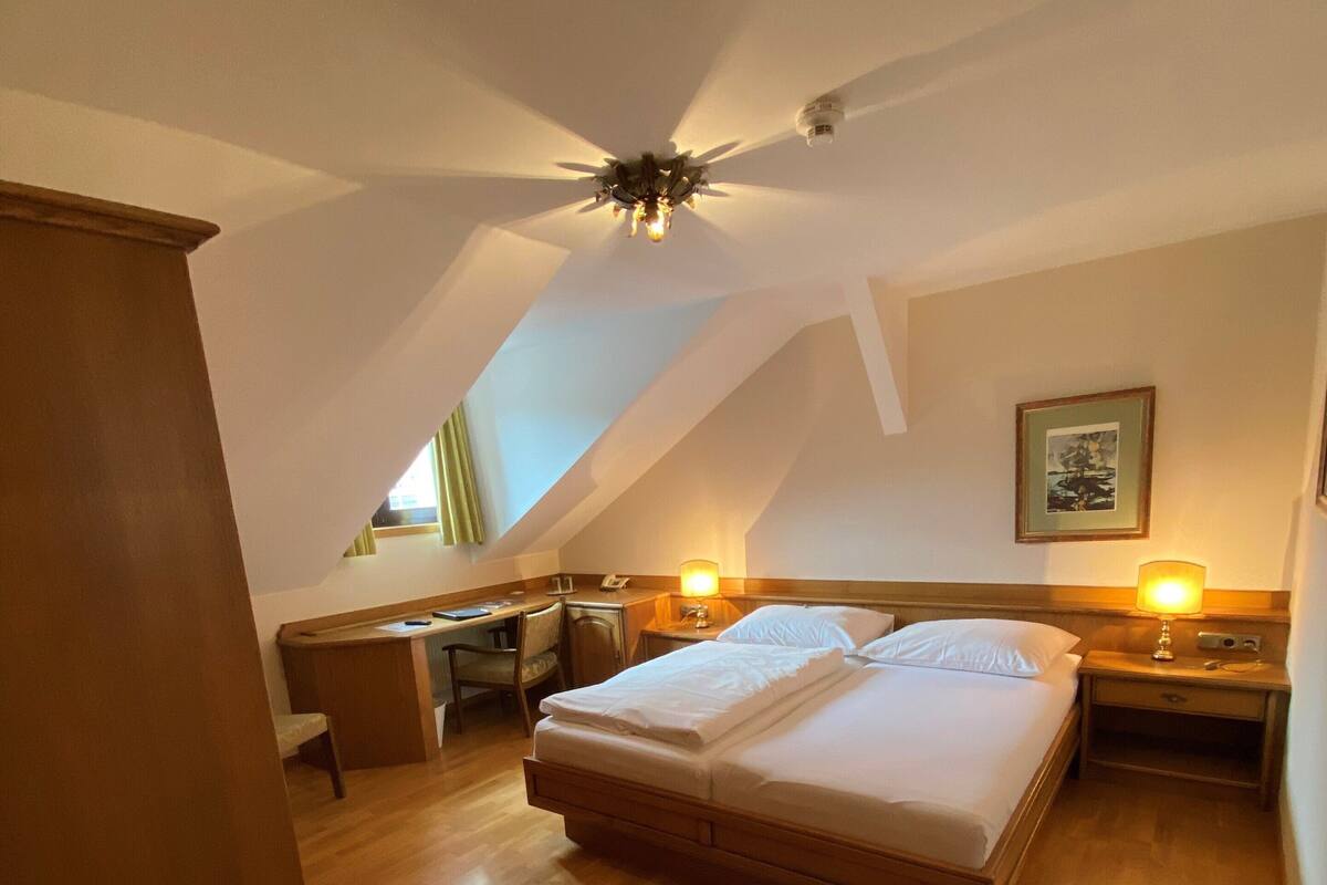 A bedroom with a bed, desk, chair, and a ceiling fan.