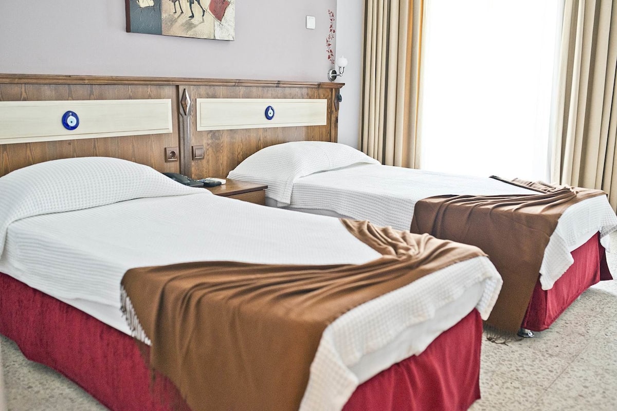 A hotel room with two beds, each with a wooden headboard, white bedding, and a brown throw blanket.