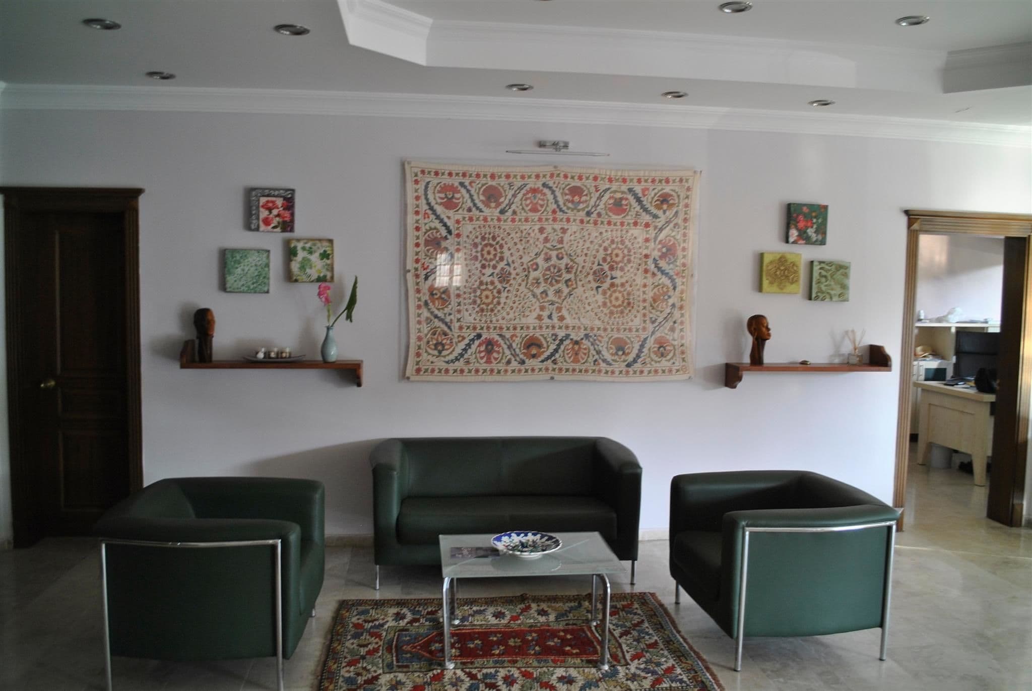 Ein Wohnzimmer mit einem grünen Sofa, zwei grünen Sesseln, einem Glastisch und einem gemusterten Teppich.