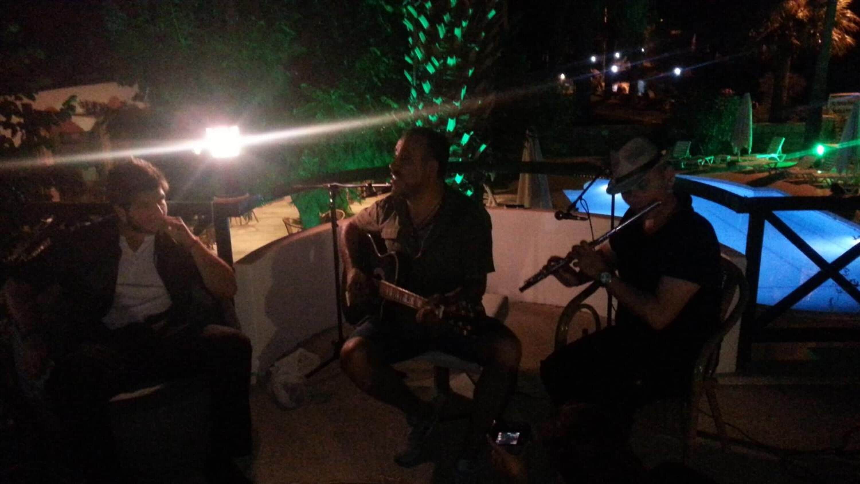 A group of people seated outdoors at night, with a pool and chairs in the background.