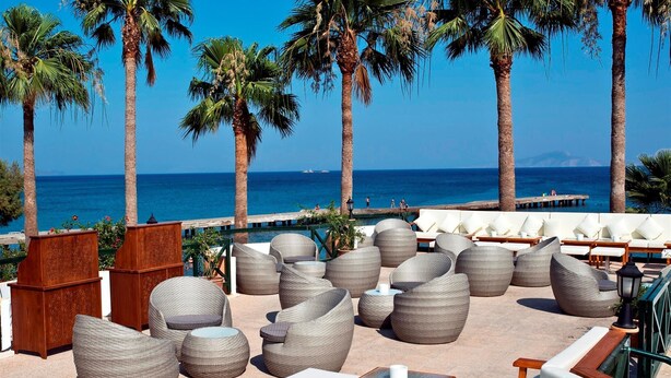 A rooftop lounge with wicker furniture, a wooden bar, and a view of the sea and palm trees. - Hotel Mare Datca (Datça)