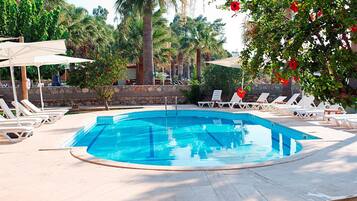 A swimming pool with lounge chairs and umbrellas, surrounded by palm trees and a stone wall.