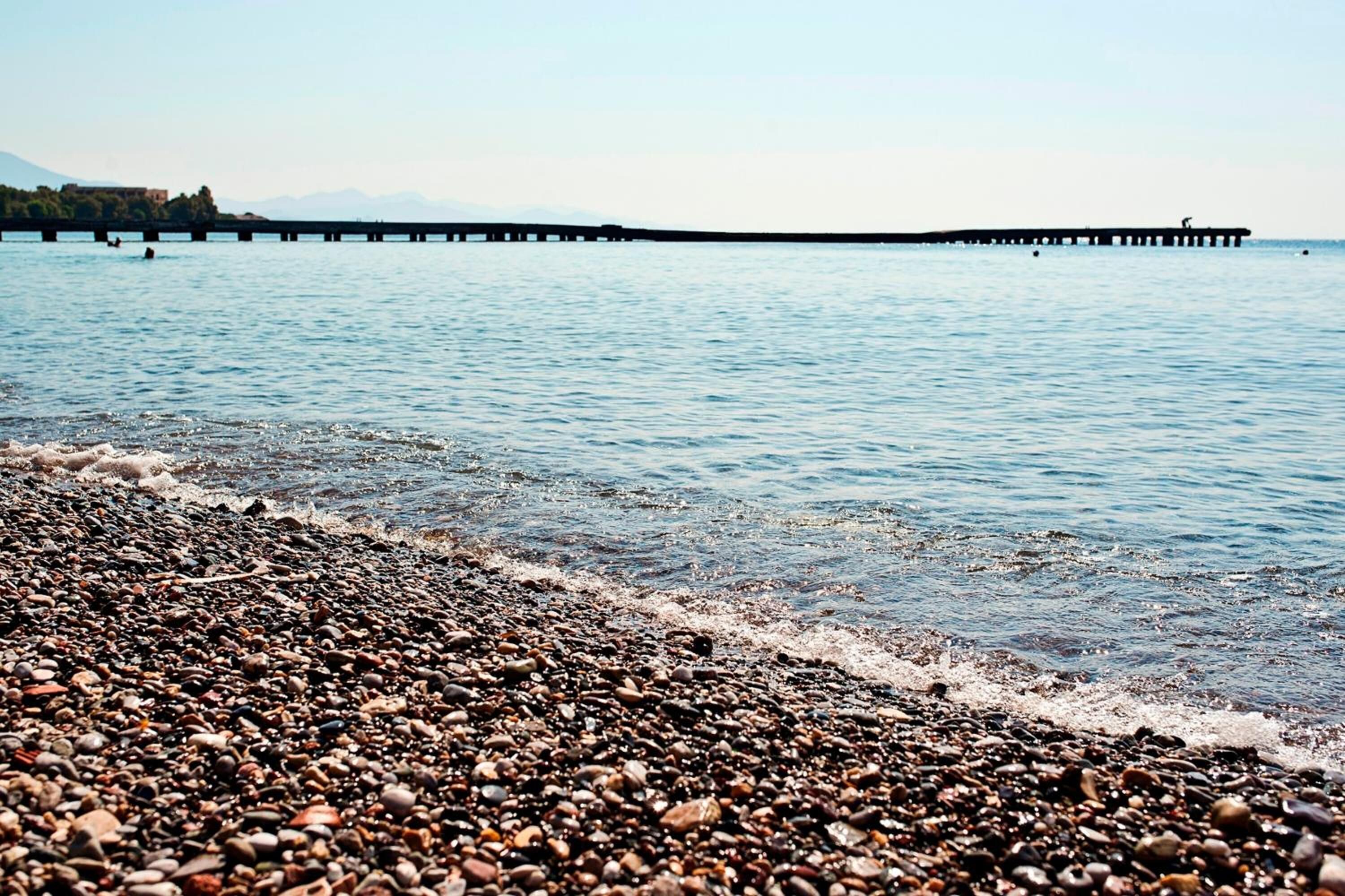 A pebbled beach with a pier extending into calm waters.