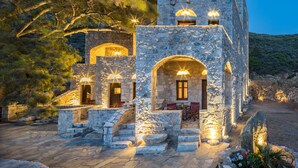 Un edificio de piedra con múltiples arcos y ventanas, que cuenta con asientos al aire libre y una escalera de piedra que conduce a la entrada.