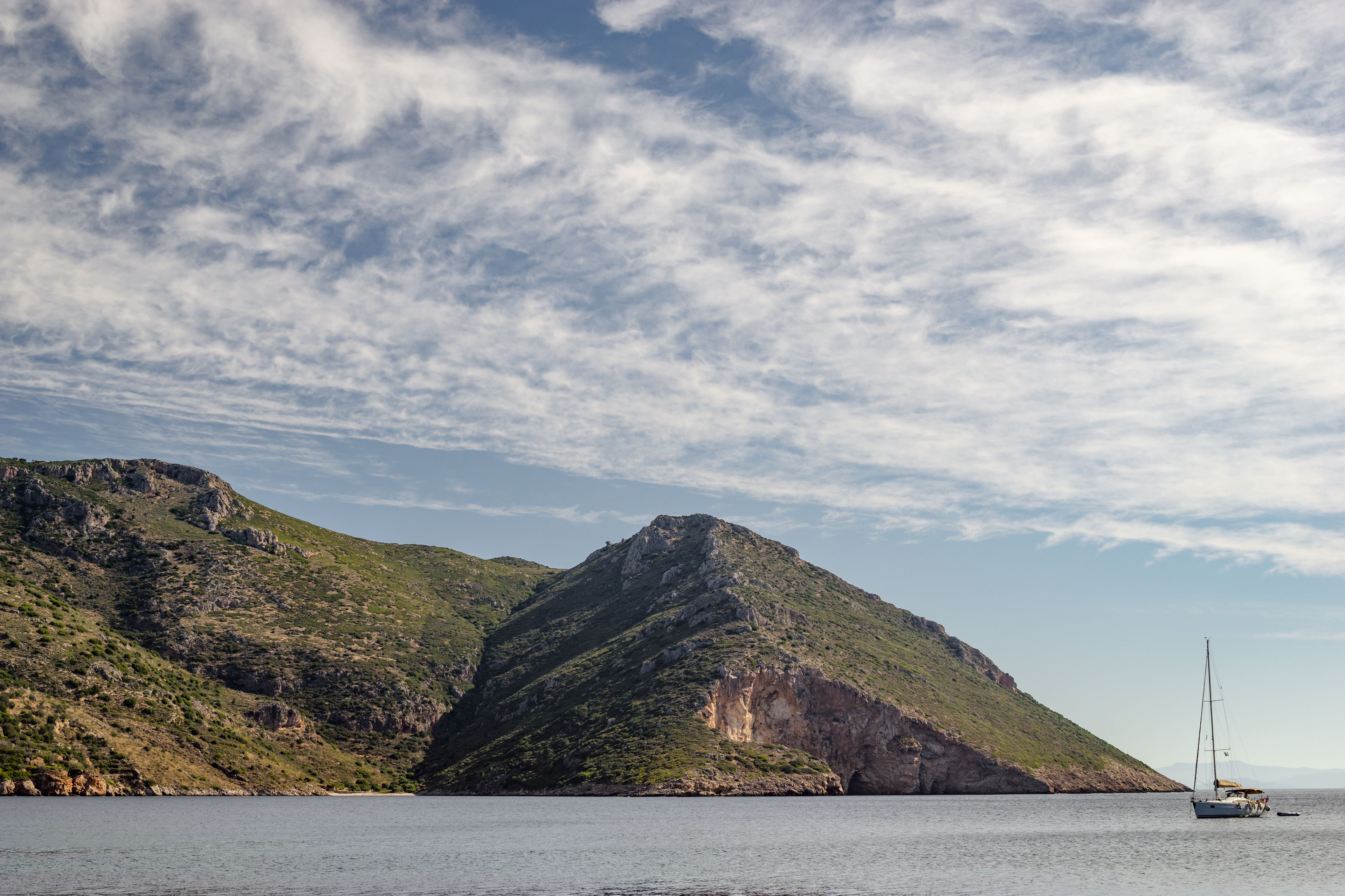 Un voilier sur des eaux calmes, avec une chaîne de montagnes en arrière-plan.