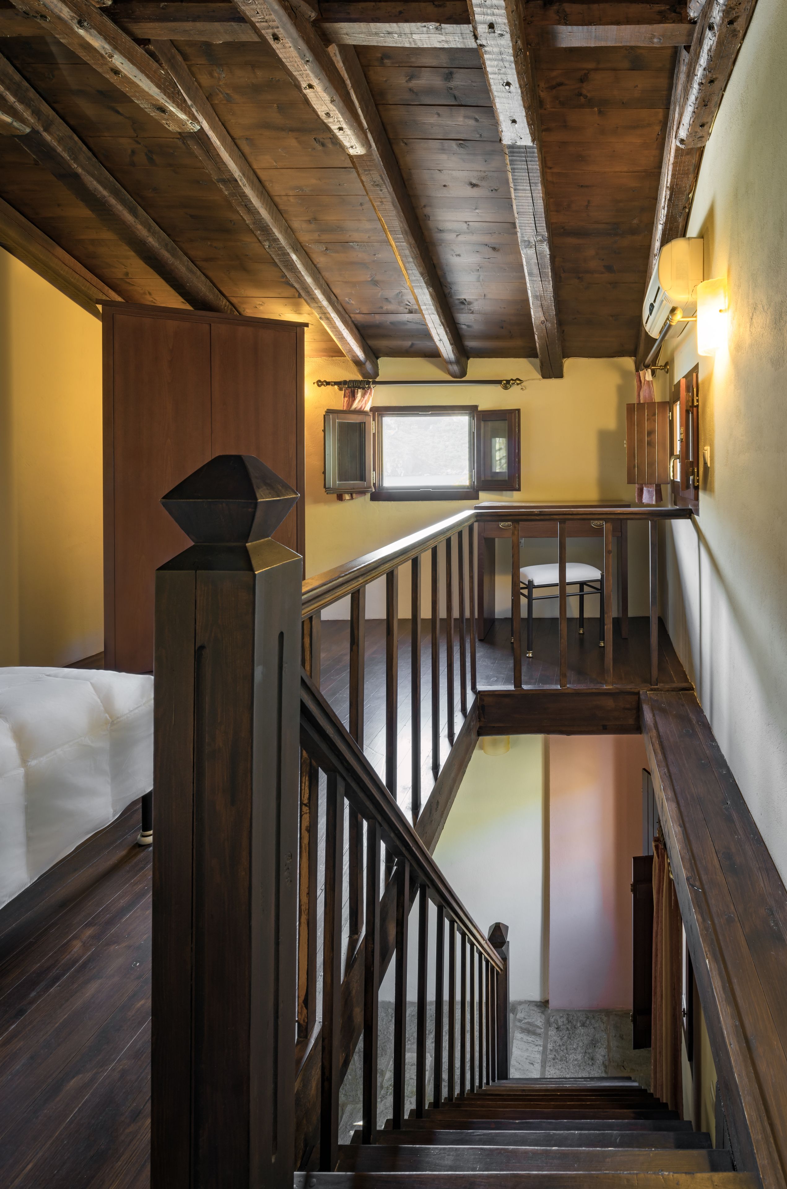 A wooden staircase with a handrail, a cushioned bench, and a television on the wall.