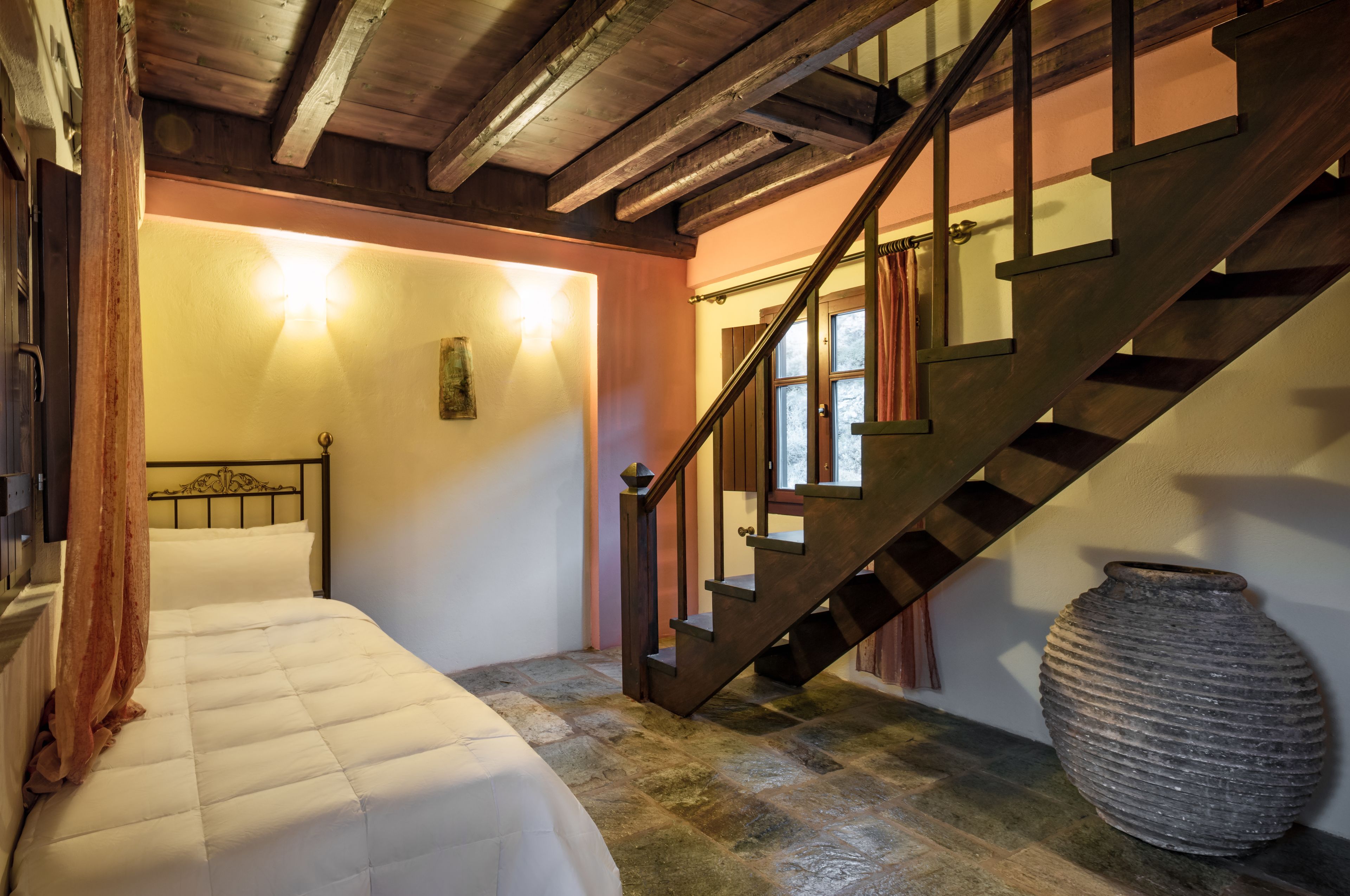 A bedroom with a bed, a wooden staircase, and a large vase.