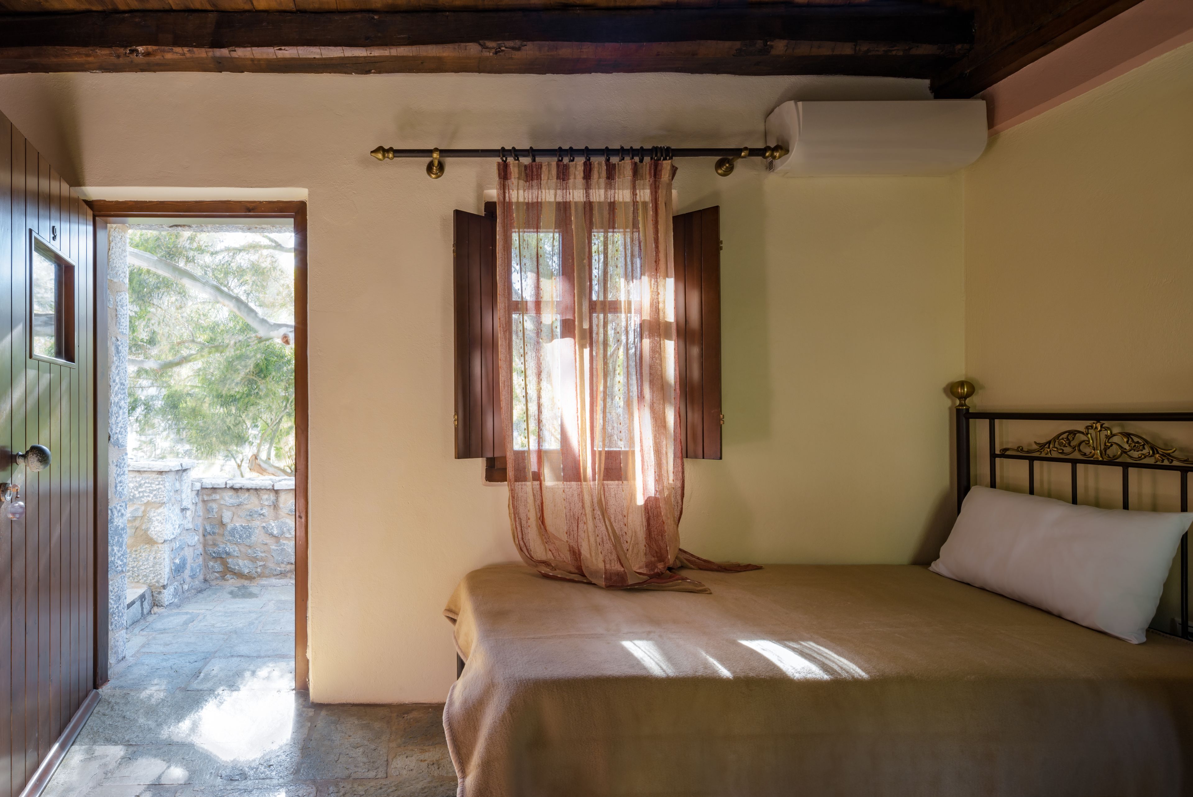 A bedroom with a bed, a window with curtains, a door, and a view of an outdoor area.