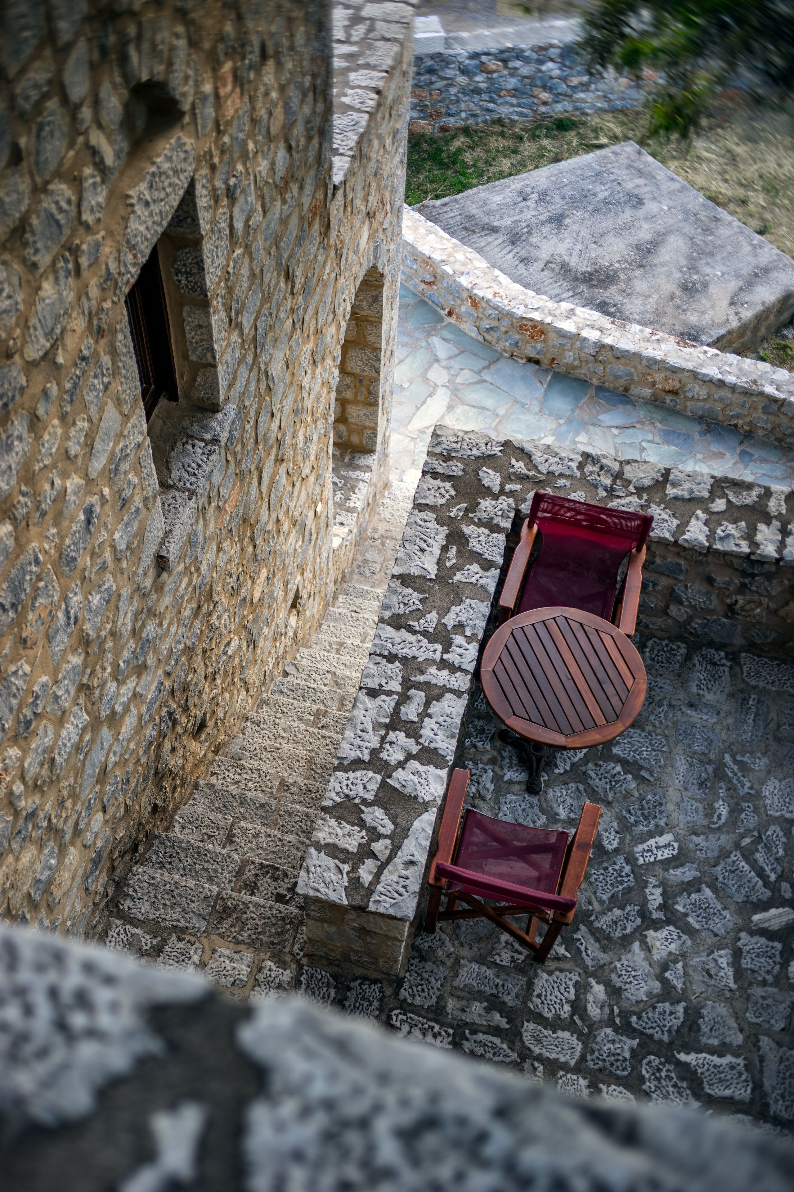 Un cortile in pietra con un tavolo rotondo in legno e due sedie, un muro in pietra e un sentiero lastricato.