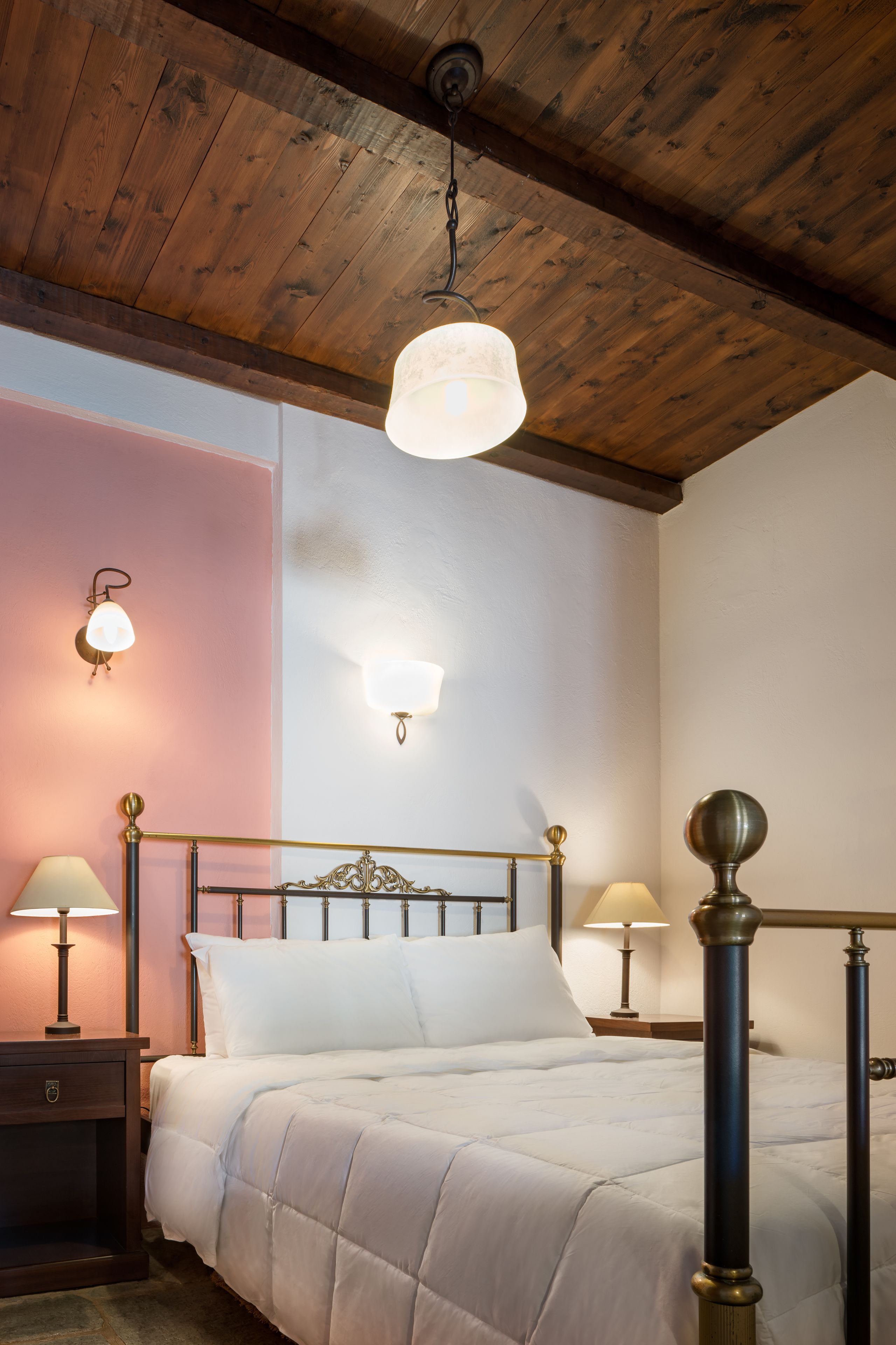 Une chambre avec un plafond en bois, un lit avec une literie blanche, deux lampes de chevet et des appliques murales.