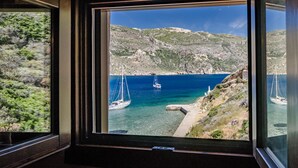 Una ventana con vista a una zona costera que muestra veleros y terreno rocoso.
