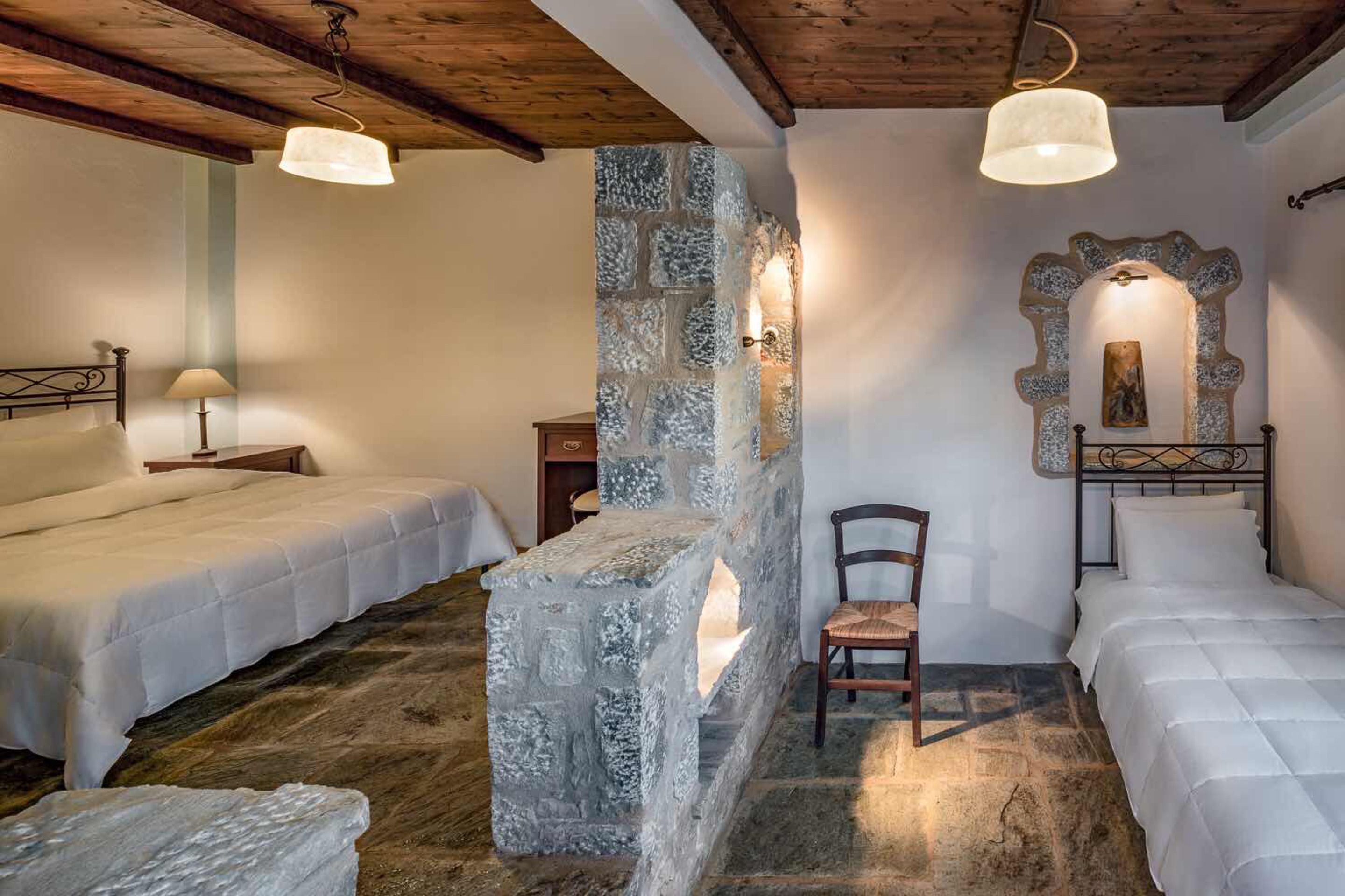 A cozy room with two beds, a stone wall, a wooden ceiling, and a stone bench.