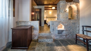 Una chimenea de piedra con un banco, un armario de madera y una cama al fondo.