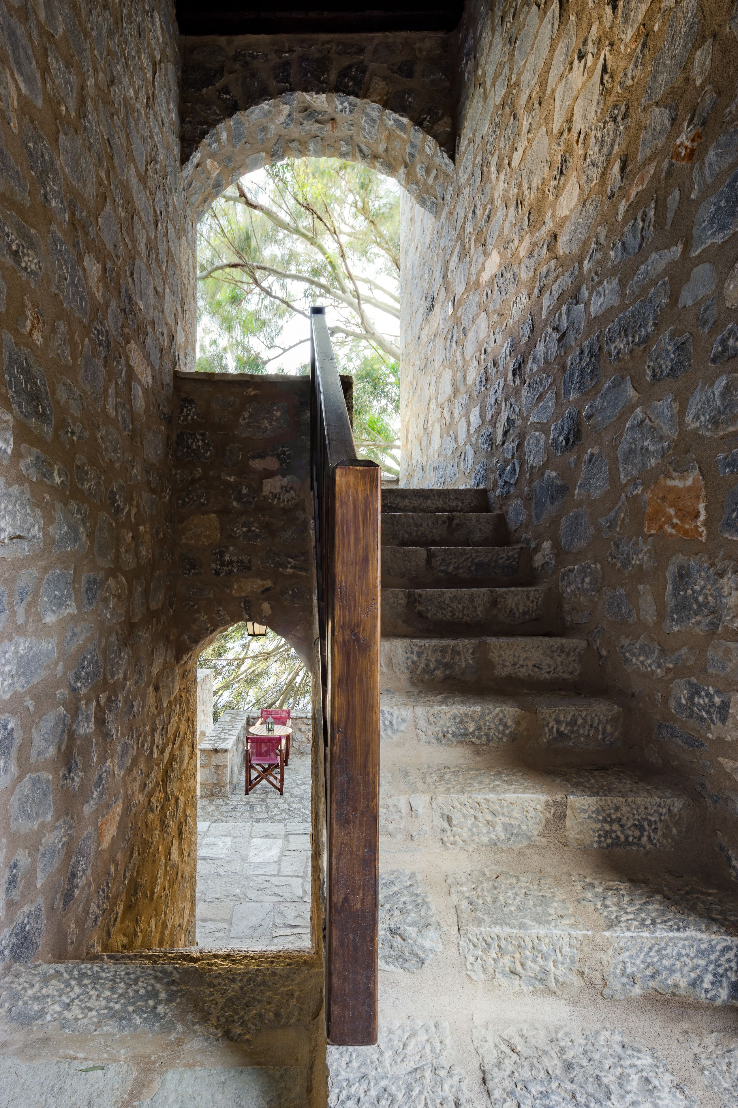 Un escalier en pierre, doté d’une rampe en bois, mène à une porte en arc de cercle.