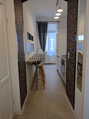 Un pasillo estrecho con una mesa de comedor y sillas, una zona de cocina con armarios y encimera, y una ventana con cortinas.