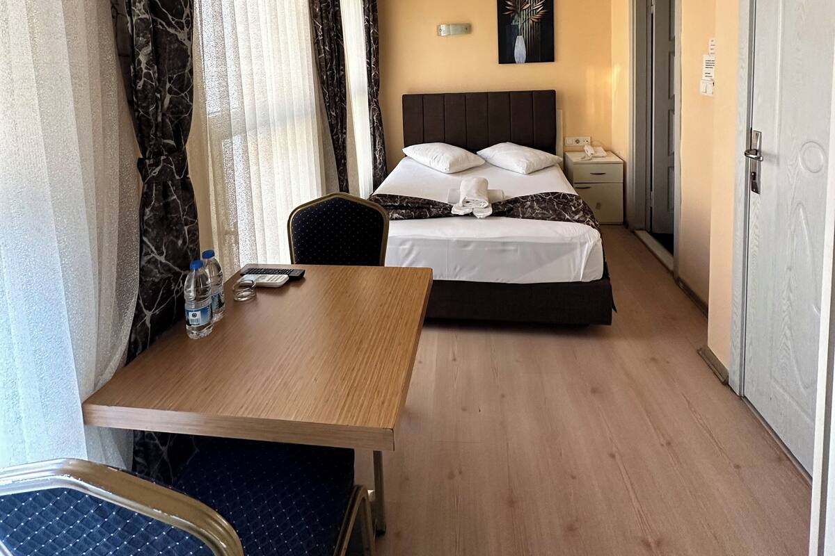Et hotelværelse med seng, skrivebord, stol, natbord og en aircondition.