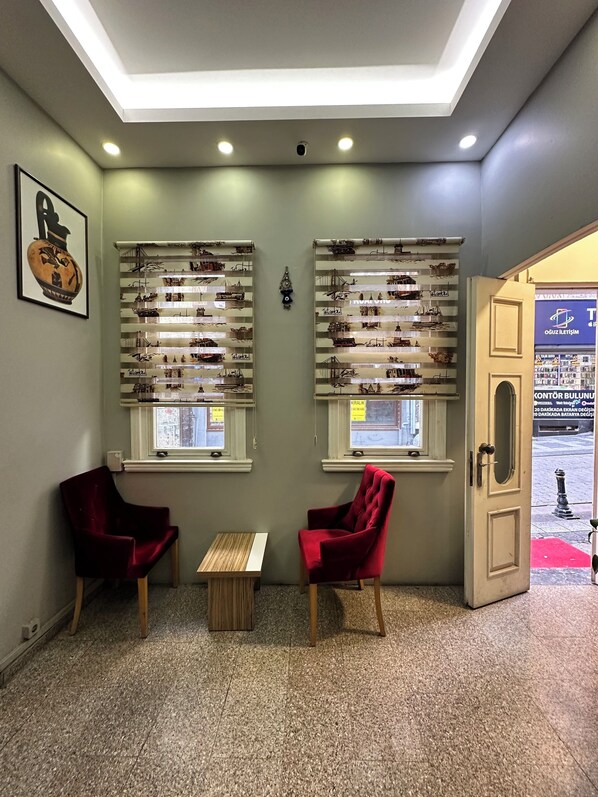 Une pièce avec deux chaises rouges, une petite table en bois et des étagères ornées d’objets décoratifs.