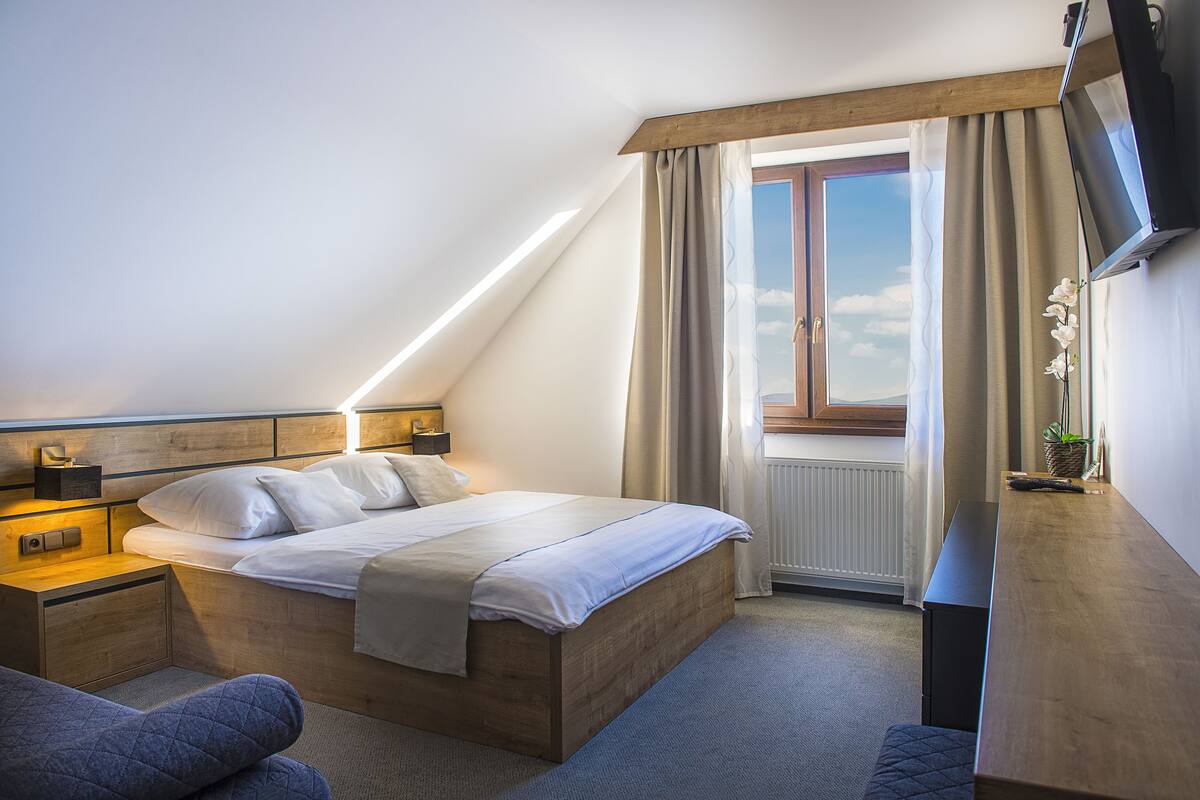 Ein modernes Hotelzimmer mit einem Holzbett, einem Nachttisch, einem Schreibtisch und einem an der Wand befestigten Fernseher.