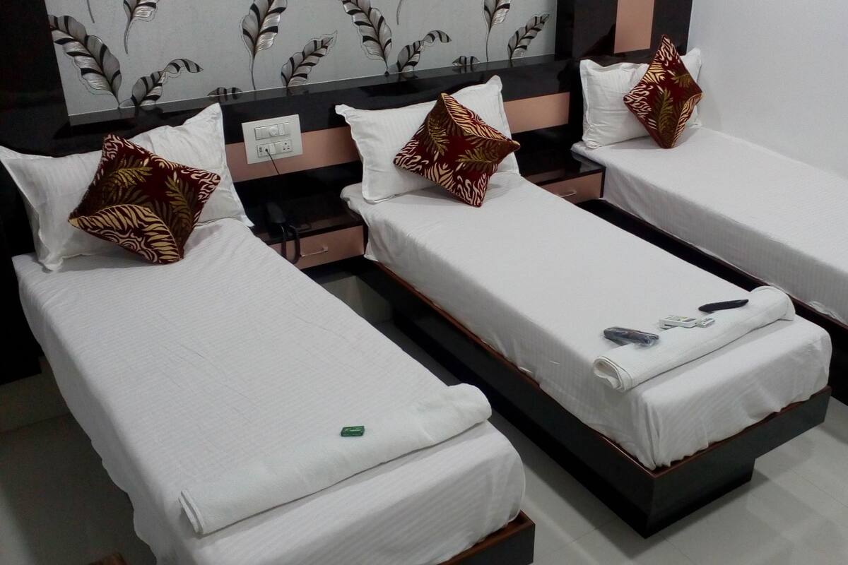 Three single beds with white linens and decorative pillows, a bedside table with a remote control, and a wall with a leaf-patterned design.