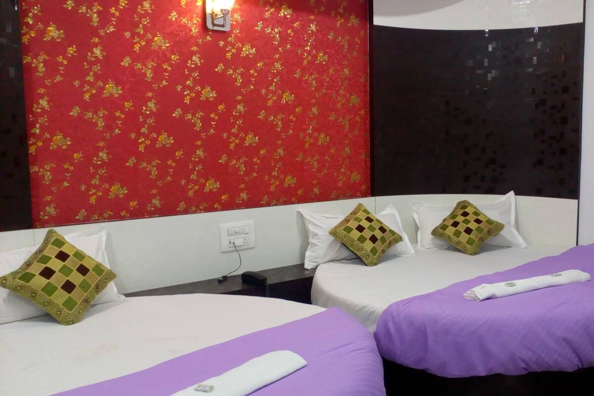 A hotel room with two beds, each with a purple bedspread and white pillows. The room has a red floral wallpaper and a black textured wall.
