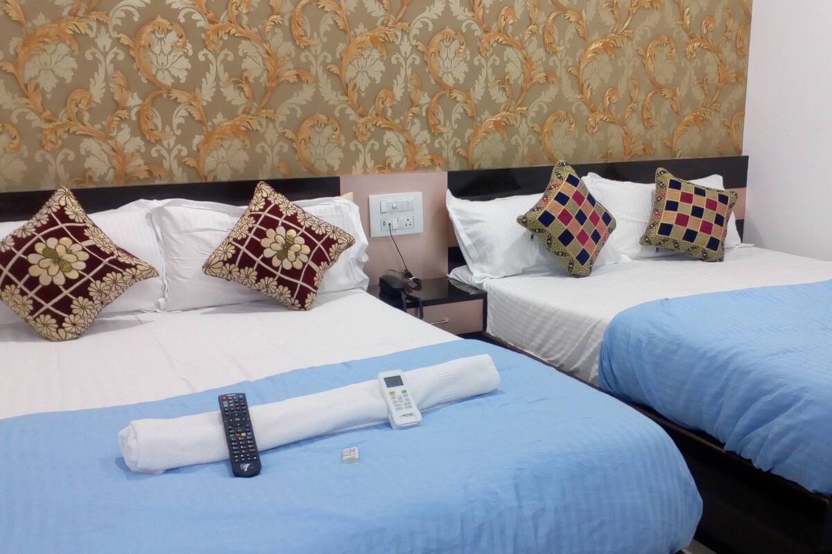 A hotel room with two beds, each with a different colored bedspread, a nightstand with a phone and charger, and decorative pillows.
