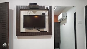 Un televisor de pantalla plana montado en la pared con marco de madera, una puerta con picaporte plateado y una vista parcial de un baño con equipo de aire acondicionado.